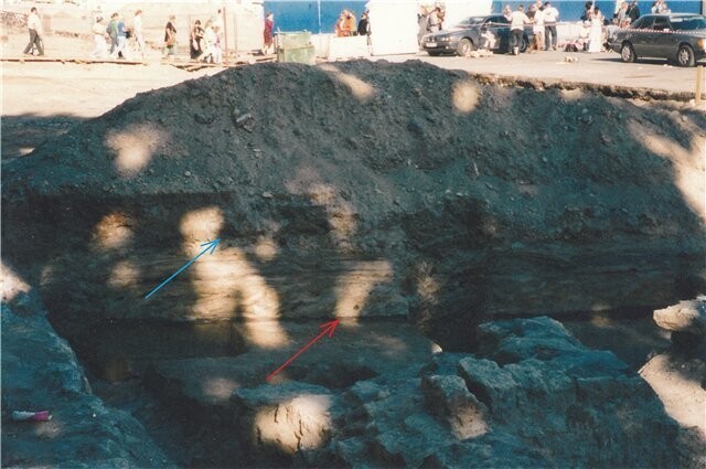 А теперь посмотрите на вот эту фотографию. Это фотография сделана в 2002 году на северо-западном углу Дворцовой площади. Красной стрелкой здесь отмечена черная полоса, которую по телевизору назвали “поверхностью времен Екатерины”.