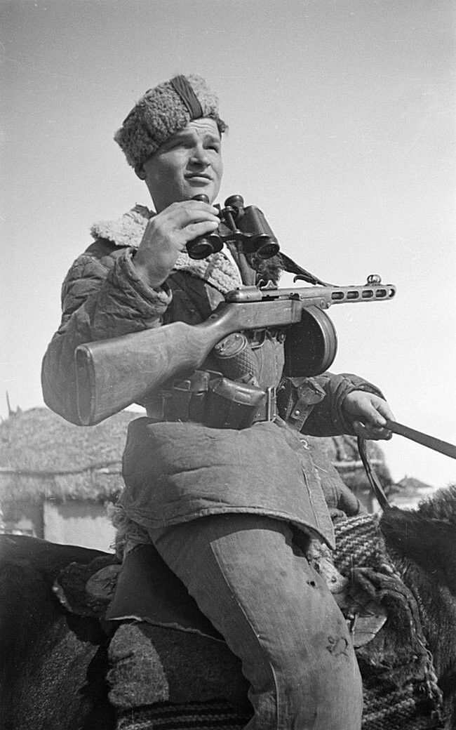 Портрет советского партизана с пистолетом-пулеметом ППШ и биноклем на коне. Время съемки: февраль 1943