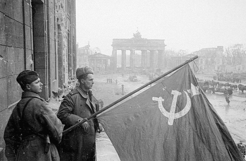 Советские военные — рядовой и лейтенант — со знаменем в Берлине на фоне Бранденбургских ворот.