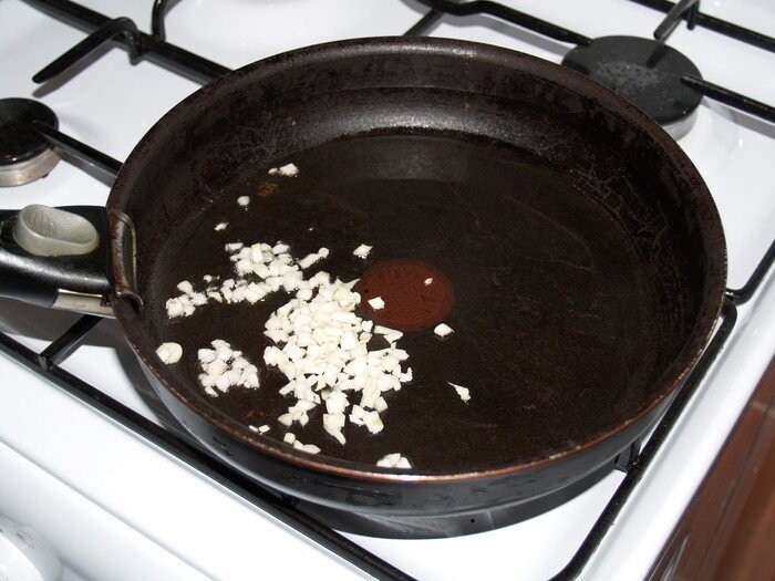 На раскалённую сковороду налейте немного растительного масла и насыпьте мелко нарезанный чеснок.