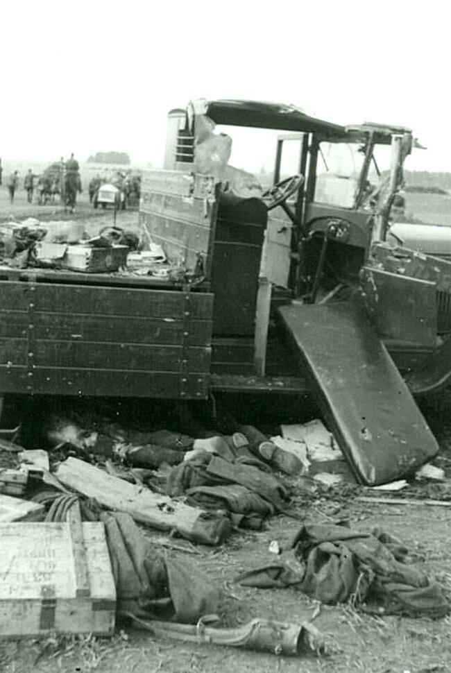 Советский грузовик-"трехтонка" ЗиС-5 с боеприпасами, разбитый в результате обстрела по дороге на Смоленск, и тела погибших красноармейцев под ним. На заднем плане — наступающие немецкие войска. Время съемки: 1941. 