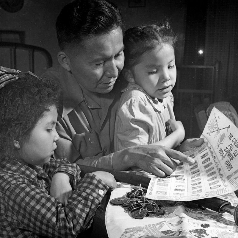 Мужчина Навахо, ветеран Второй мировой войны показывает детям свою коллекцию японских марок и монет. 1948