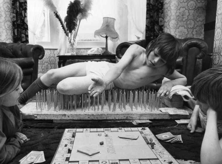 10-летний Марк играет в "Монополию", лежа на ложе из гвоздей. Лондон, 1976 год