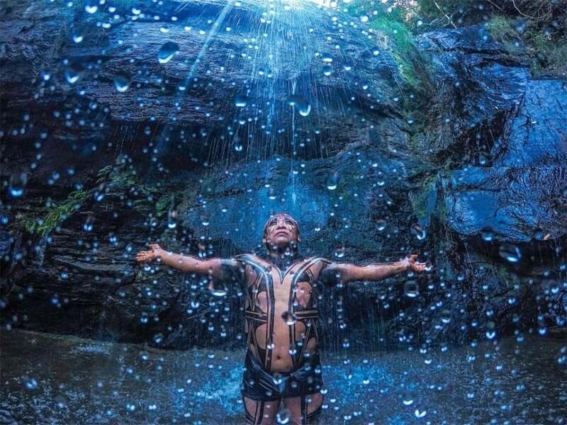 Индеец из племени Yawalapiti стоит под водопадом в национальном парке Шапада-дус-Веадейрус