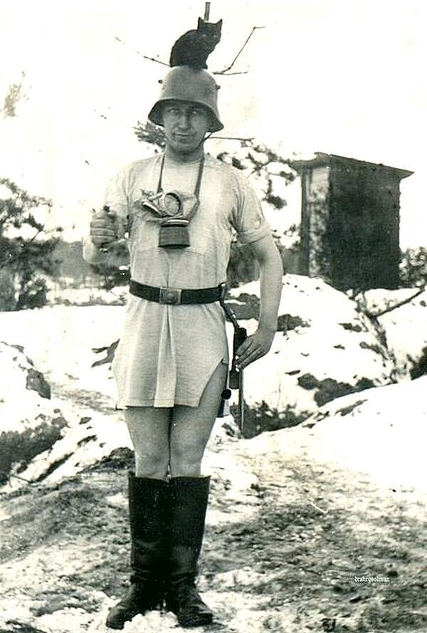 Немецкий солдат в ночной рубашке и сапогах, с котом на шлеме. 1940-ые годы.