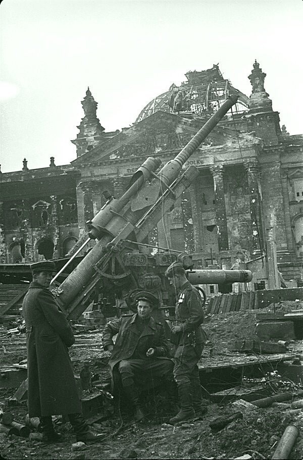 46. Советские военнослужащие отдыхают возле разбитого немецкого 88-мм зенитного орудия Flak 37 у здания Рейхстага в Берлине.