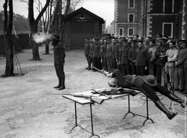 Капитан Джордж Эш лежа на спине, стреляет по глиняной трубке которую держат в зубах. 1932