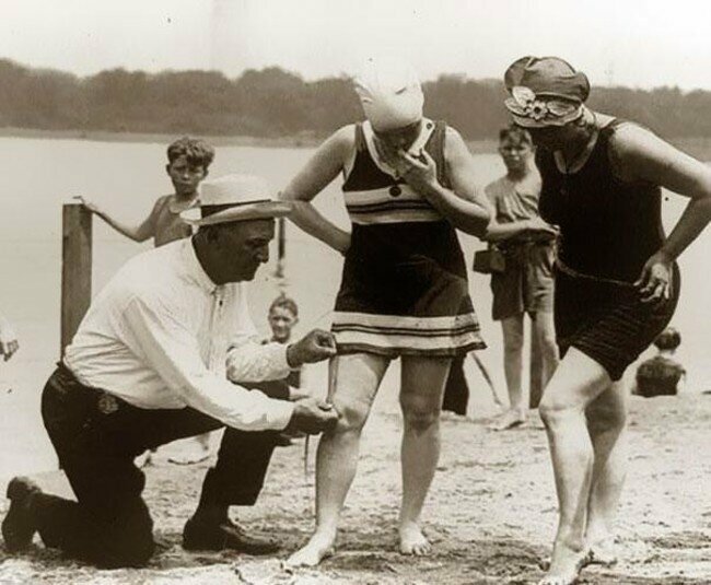 Официальный измеритель купальников на пляже проверяет, не слишком ли они коротки (1920). 