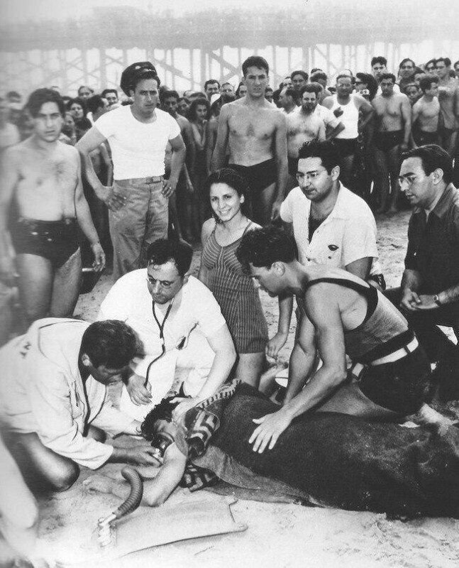 Врачи делают искусственное дыхание утопленнику,а девушка в купальнике позирует на камеру. Нью-Йорк, 1940 год.