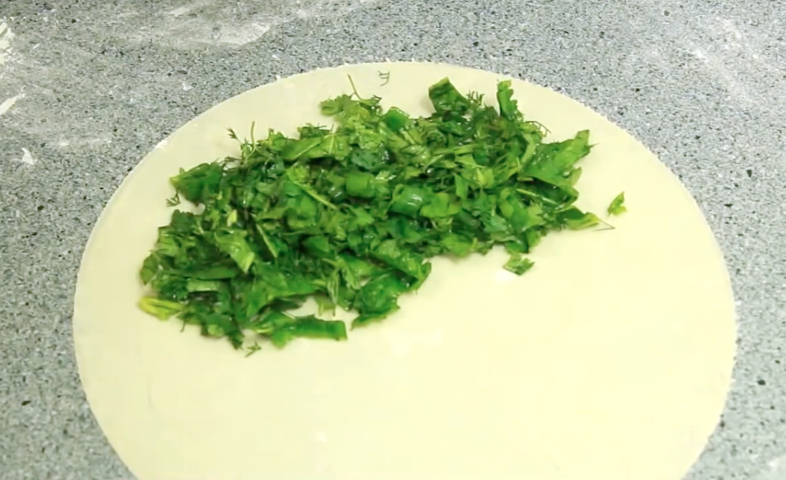 Тесто делим на части и раскатываем в тонкие лепешки. На каждую половину лепешки выкладываем зелень и солим по вкусу, накрываем второй половиной лепешки и хорошенько закрепляем края.