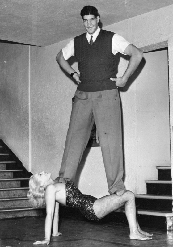 Боксер Ewart Potgieter стоит на силовой актрисе цирка Джоан Роудс, 1955