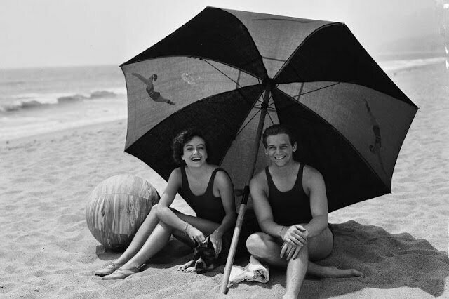 Молодожены Джоан Кроуфорд и Дуглас Фэрбенкс отдыхают со своей собакой в тени пляжного зонтика на пляже Каталина, 1929. Фото Джорджа Рейнхарта.