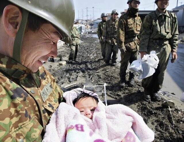 Солдат самообороны Японии улыбается, держа на руках ребенка, пережившего разрушительное цунами, 2011 год
