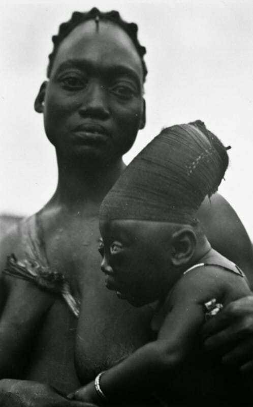 Мать из племени мангбету держит своего сына, которому удлиняют череп согласно традициям. Конго, 1950 год 