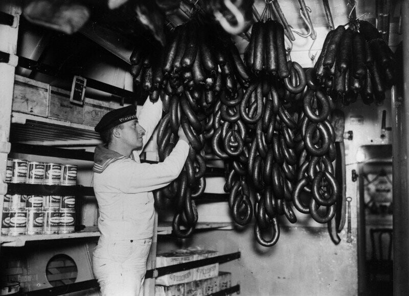 Немецкий моряк осматривает колбасы, висящие в провизионной на корабле. Германия 1936г.