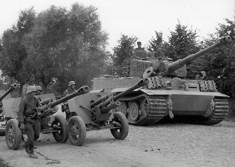 Танк «Тигр» (Pz.Kpfw. VI Ausf. E Tiger) панцер-гренадерской дивизии «Великая Германия», проезжает рядом с советскими 76-мм орудиями ЗИС-3 по улице городка Вилкавишкис. Литва, осень 1944 года.