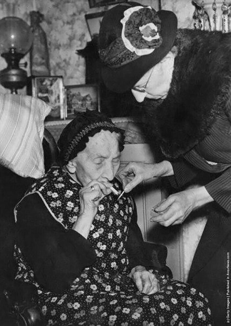 75-летняя Мэри Пэриш прикуривает сигарету для ее 101-летней матери, Мэри Энн Пэриш. Валворт, Лондон, 14-го февраля 1946 года.