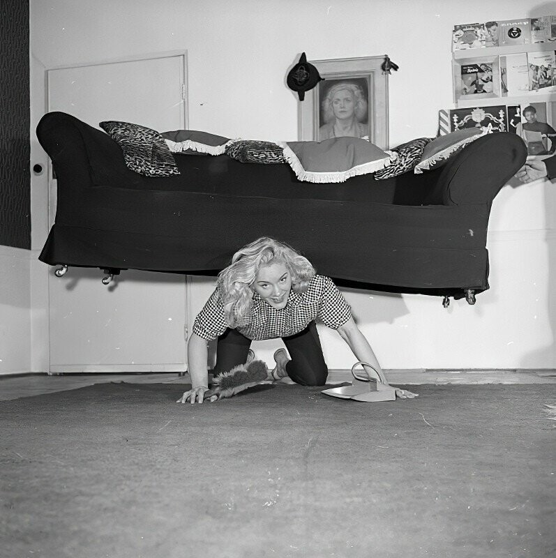 Английская цирковая силачка мисс Джоан Роудс поддерживает себя в форме занимаясь уборкой у себя в квартире, 1958 год.