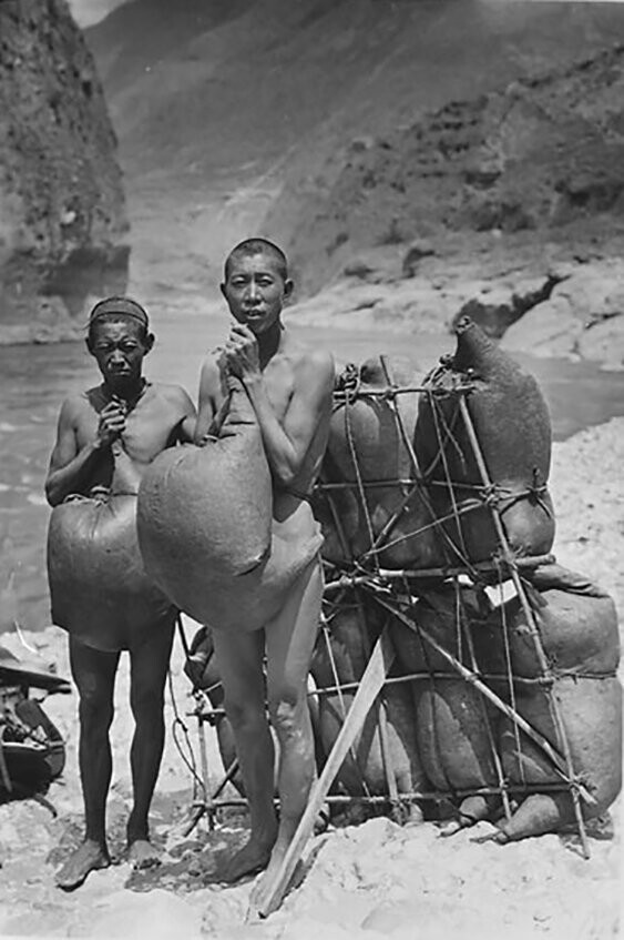 Два пловца-наси, носящие надутые козьи шкуры, стоят рядом с плотом из козьей шкуры, который используется в качестве парома для переправы через реку Янцзы из За-ба в Та-ку, 1925
