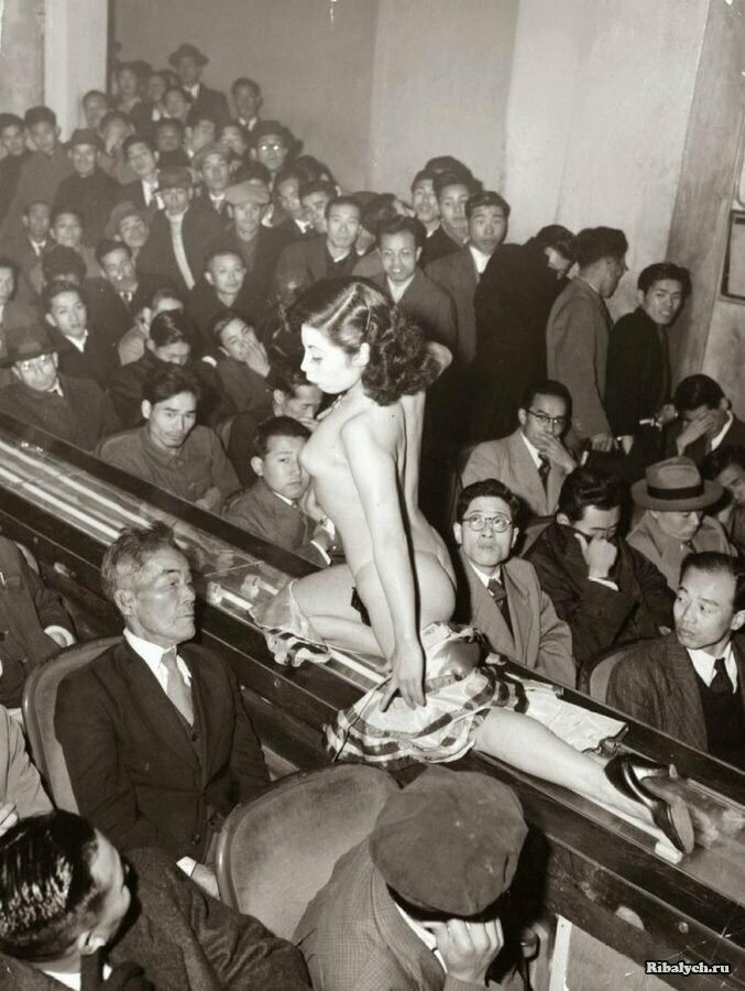 Участница стриптиз шоу проезжает мимо зрителей на конвейерной ленте. Токио, 1957 год 