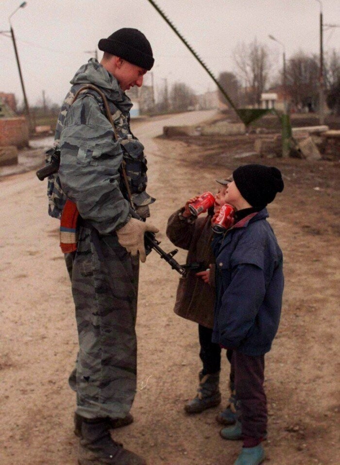 15. Солдат федеральных сил угощает чеченских ребят кока-колой, 1996 год