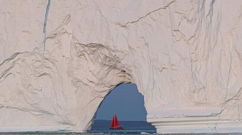 Крошечная лодка проплывает возле огромного айсберга