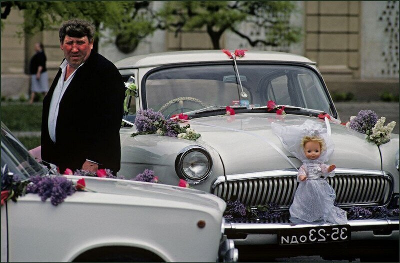 Водитель со своей машиной, украшенной свадебными цветами и куклой, ждет жениха и невесты после их свадьбы. Одесса, Украина, 1982. Автор фото: Иэн Берри.