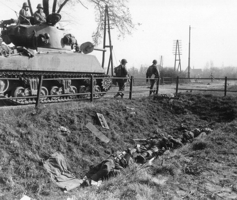 Танкисты на танке M4A3(76)W «Sherman» проезжают мимо убитых немецких солдат подразделения истребителей танков в районе Гановера. 10 апреля 1945 года. Германия.