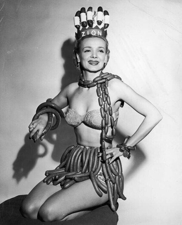Актриса Джин Кортни демонстрирует шарф, юбку, браслеты и корону из хот-догов, сосисок и колбасы в роли королевы национальной недели хот-догов, выбранной компанией Zion Meat Products Company, 1955 год