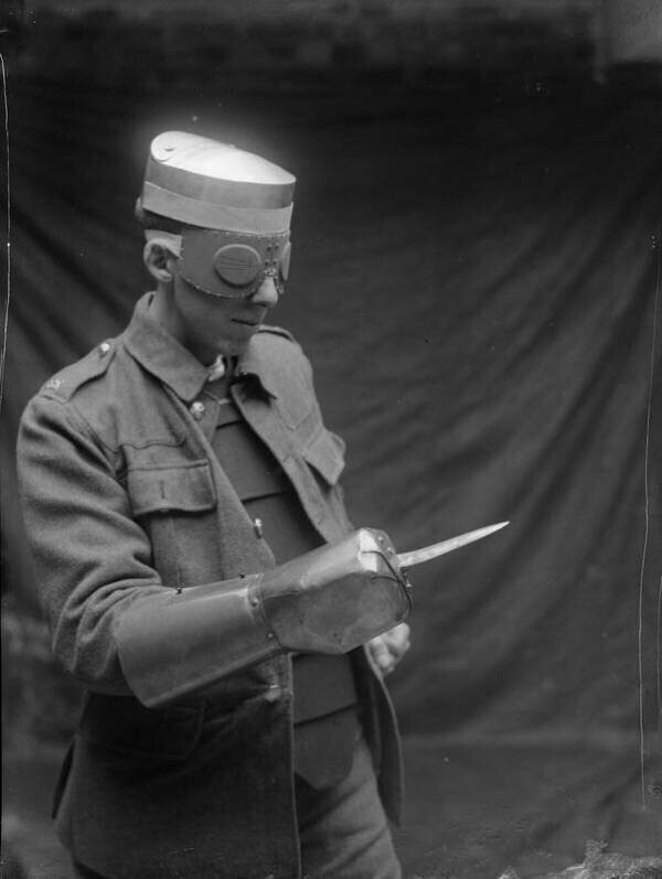 Мужчина демонстрирует шлем, очки и стальную перчатку с кинжалом, изготовленную для британских военных во время Первой мировой войны