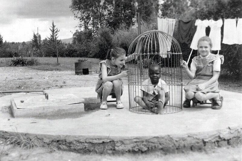 Две белые девочки играют с негритёнком в клетке для птиц, Бельгийское Конго. 1955