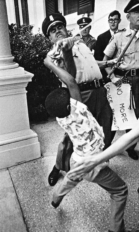 Полицейский вырывает американский флаг у 5-летнего Энтони Куинна, уже конфисковав его знак «Нет больше жестокости полиции». Джексон, Миссисипи. 1965 год