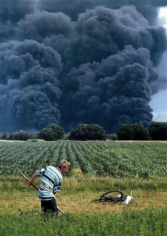 Мужчина косит в поле на фоне горящего нефтеперерабатывающего завода в Панчево, Сербия, 1999 год
