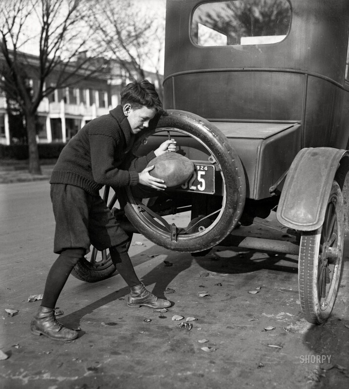 Мальчик надувает мяч от запасной шины автомобиля. США, 1924