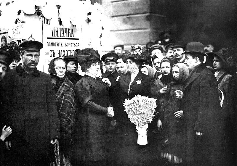 Сборщица прикрепляет значок участнице сбора средств на борьбу с чахоткой в "День белого цветка".