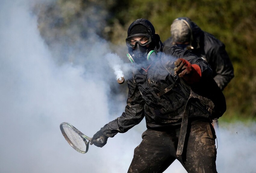 Протестующий использует теннисную ракетку, чтобы бросить баллон слезоточивого газа во время операции по эвакуации французскими жандармами в зоне ZAD (Зона отложенного развития) в Нотр-Дам-де-Ланд, недалеко от Нанта, Франция, 11 апреля 2018 года.