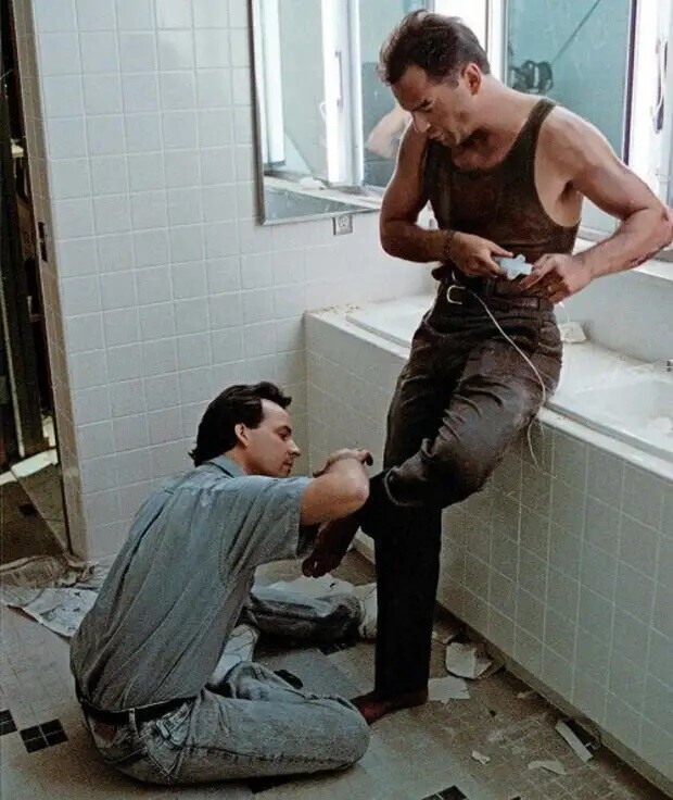 Скотт Х. Эддо мажет поддельной кровью ногу Брюса Уиллиса на съёмочной площадке фильма "Крепкий орешек"