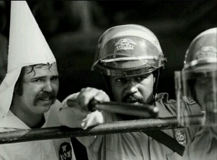 Чернокожий полицейский защищает членов расистской организации KKK от протестующих, 1983 год.