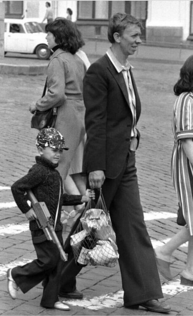 Советский мальчик с игрушечным пулеметом идет по Красной площади с отцом, держась за авоську с товарами.