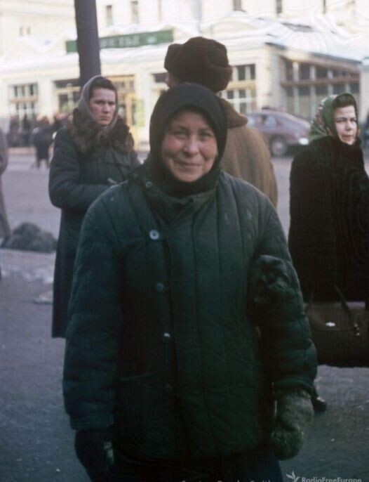 Советская женщина в телогрейке и тёплых рукавицах позирует фотографу на улице в морозный день.
