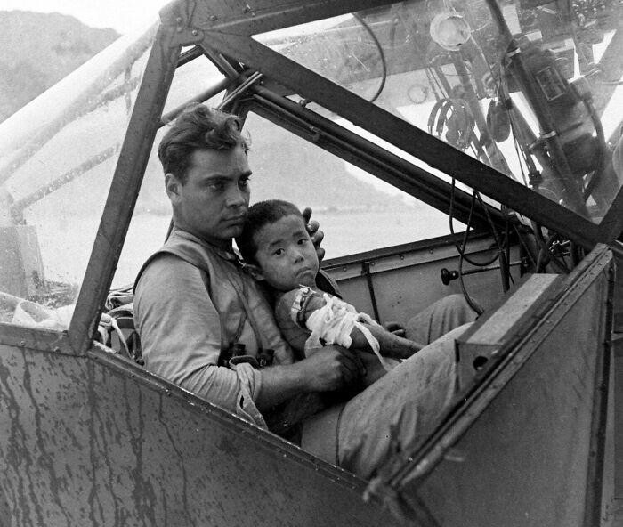 15. Американский солдат укрывает от дождя раненого японского мальчика в кабине самолета во время битвы за Сайпан, ожидая его транспортировки в полевой госпиталь. Июль 1944 года