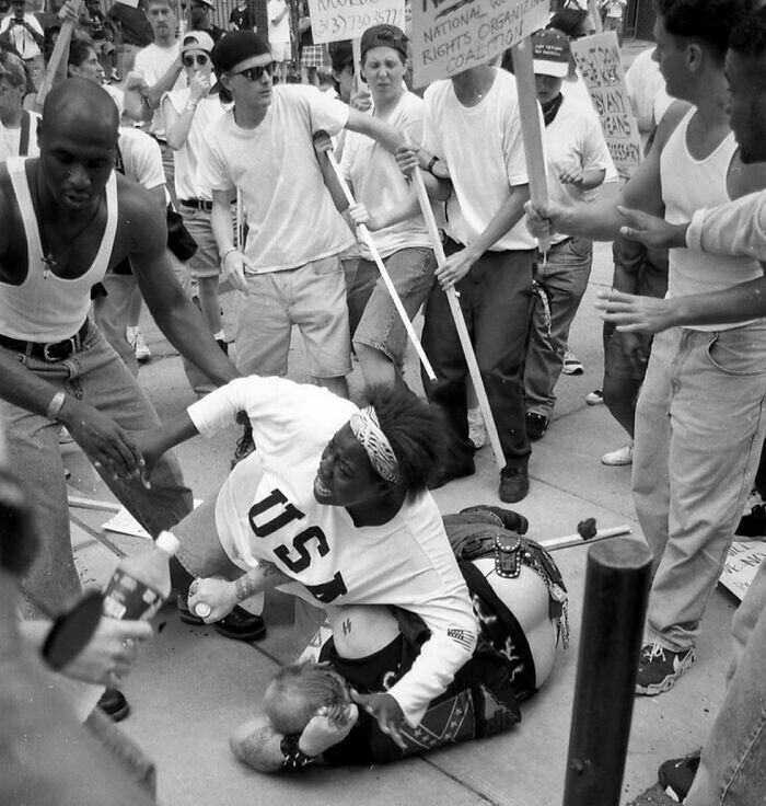 18-летний Кешия Томас защищает павшего человека, предположительно связанного с Ку-клукс-кланом, от разъяренной толпы антиклановых протестующих. Анн-Арбор, Мичиган, США. 1996 Марк Бруннер