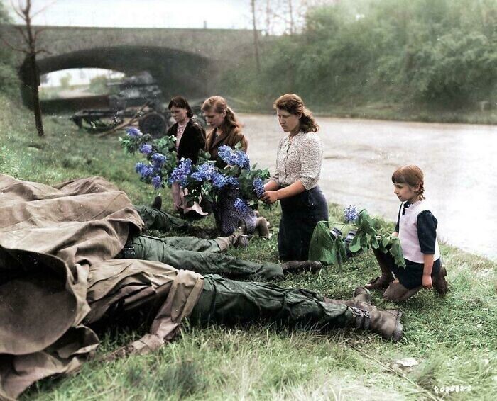 Три молодые русские женщины и маленькая девочка, недавно освобожденные армией США из лагеря рабского труда, возлагают цветы к ногам четырех мертвых американских солдат. 18 апреля 1945 года, Хильден, Германия.