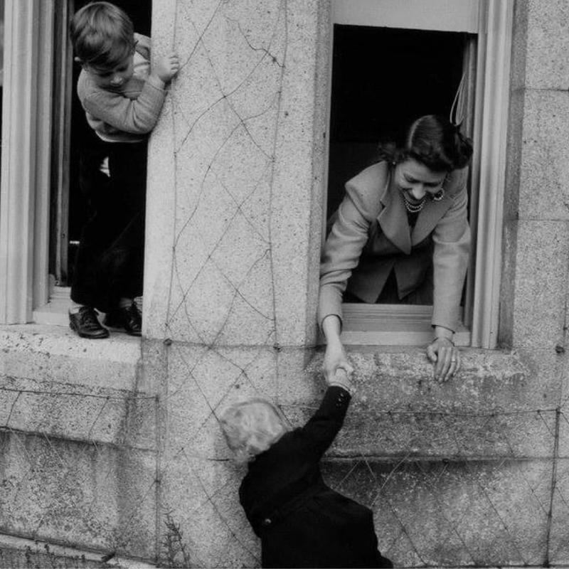 Принц Чарльз наблюдает, как королева Елизавета помогает принцессе Анне забраться в окно замка Балморал в Шотландии, 1952