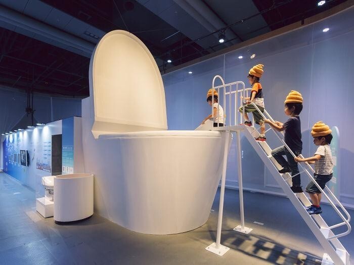 30. Дети в шляпах в форме какашек спускаются в гигантский туалет. Выставка в Токио