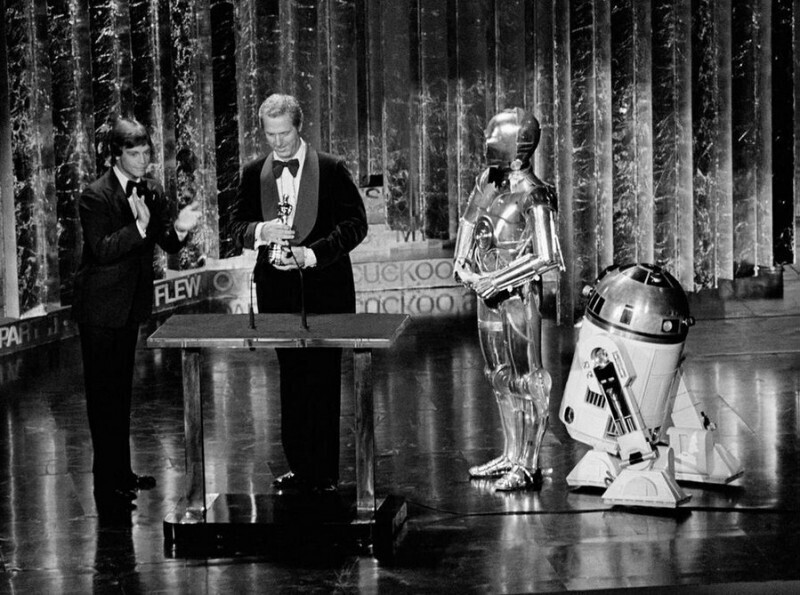 50-я церемония вручения Оскара. Марку Хэмиллу (Люку Скайуокеру из «Звёздных войн») помогают С-3РО и R2-D2 во врем вручения награды за особые достижения в звуковых эффектах. R2-D2 постоянно перебивал, смеша публику. Голливуд. США. 3 апреля 1978 г.