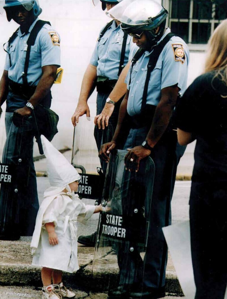 Ребенок в одеянии Ку-клукс-клана видит свое отражение в защитном щите полицейского, штат Джорджия, США, 1992 год