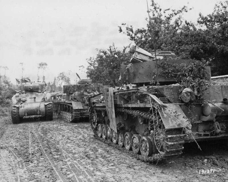 Американский средний танк М4А1 из состава американской 2-й бронетанковой дивизии проезжает мимо двух подбитых немецких танков Pz.IV.