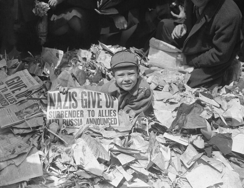 Мальчик показывает вырезку из газеты: "Нацисты сдаются. Союзникам и России объявлено о капитуляции", 1945 год.