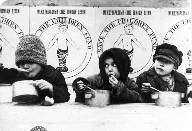 Детей кормят по программе «Спасите детей» - части международной кампании по обеспечению пропитанием не менее 7 миллионов детей-сирот, рожденных русской революцией. Саратов, 1921 года.